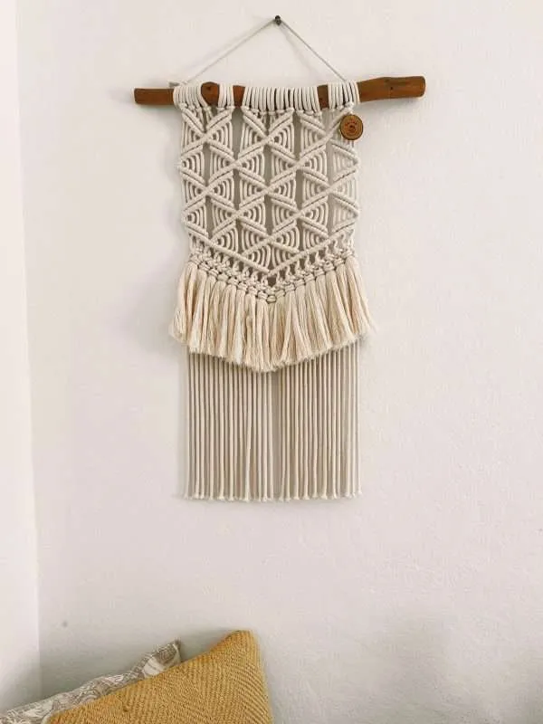 Painel de parede em macramé Blossom com rede de losangos e franja dupla, numa parede branca